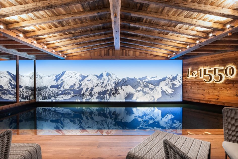 Indoor pool at Chalet Le 1550, Courchevel Village Interior pool of Chalet Le 1550 in Courchevel Village, surrounded by traditional alpine wood and a screen displaying mountain scenes.