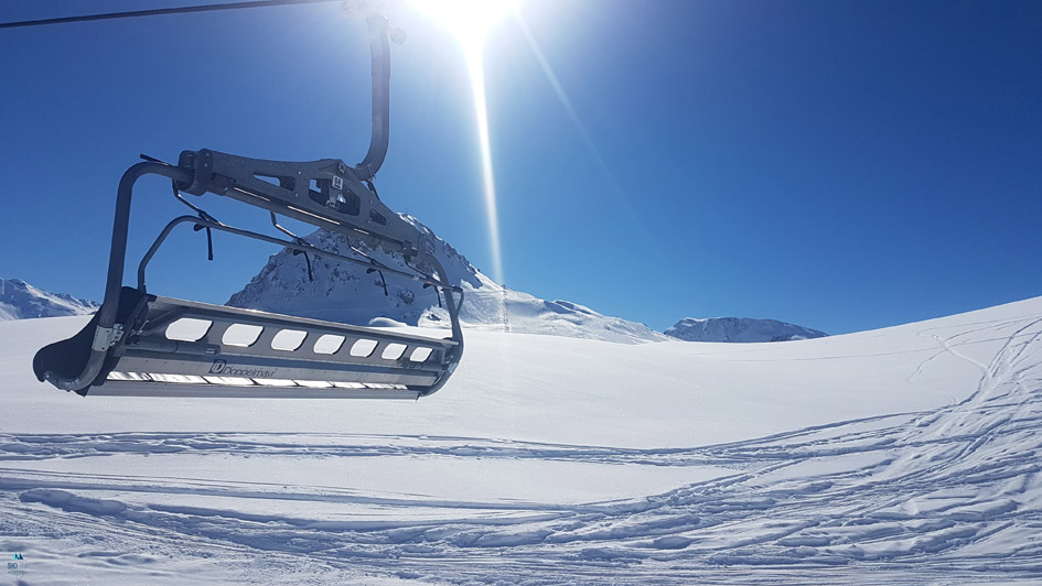 A chairlift will transport you up the mountain on a bluebird ski day, and will transport you to the slopes when set as a free ski Zoom background.