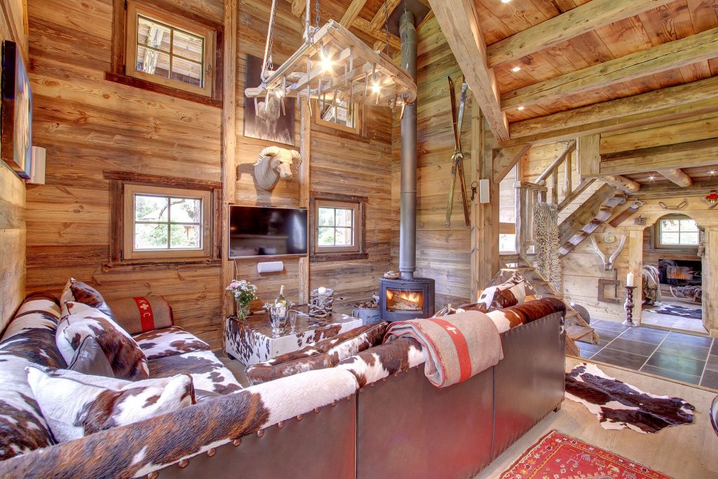La Petite Ferme, Morzine Typically, alpine living room with cow style sofas and classic wooden beams surrounding a log burner at luxury self catered chalet in Morzine