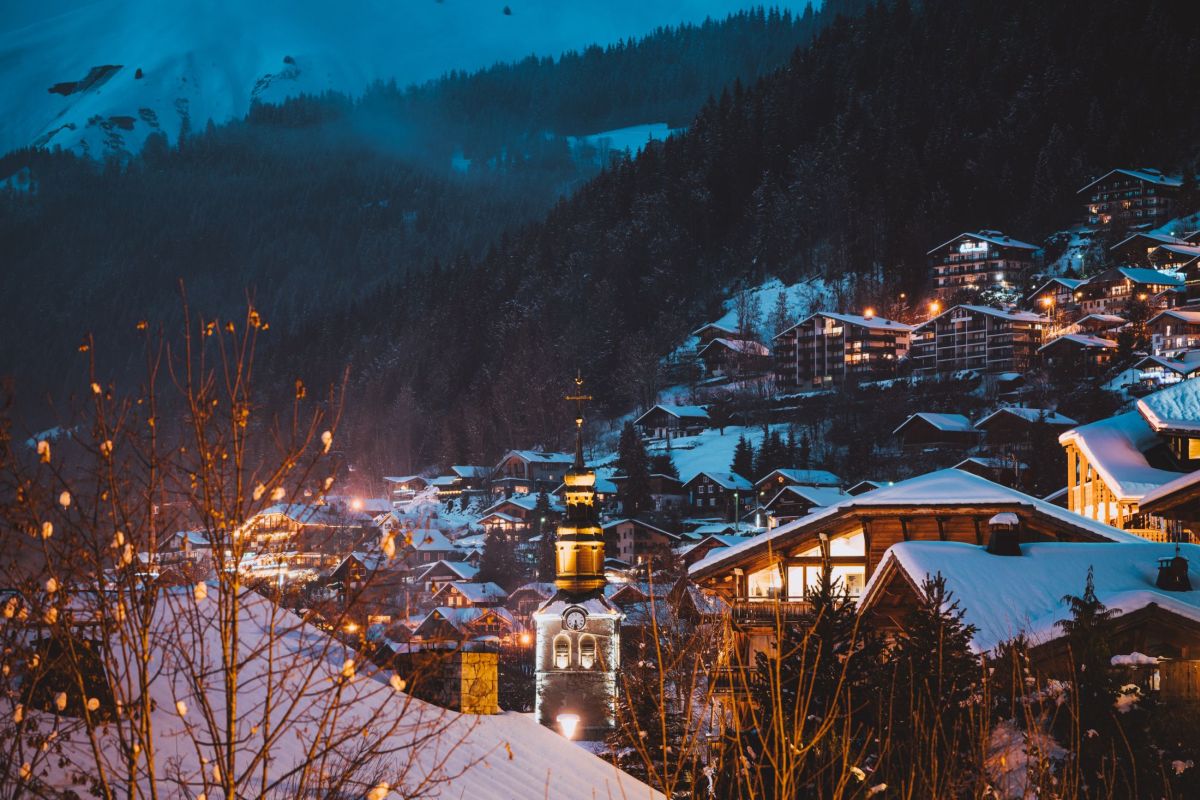 ski resort Morzine by night featuring beautiful lit chocolate box chalets and snowy mountains lined with trees 