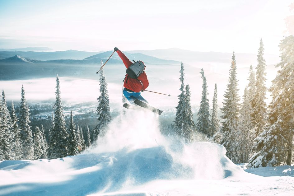 A skier leaping off a powder jump, skiing without fear towards the snowy mountain forest.