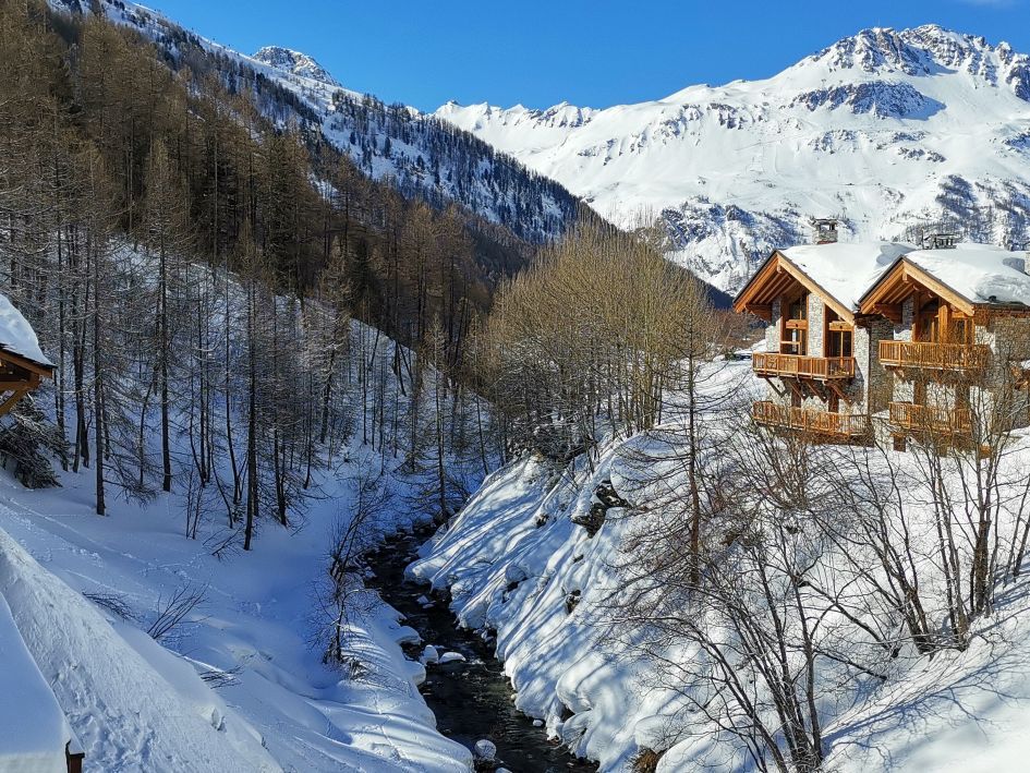 An external shot of Chalet Oxalis in Le Fornet, Val d'Isère, with the river running by at the base of its garden.