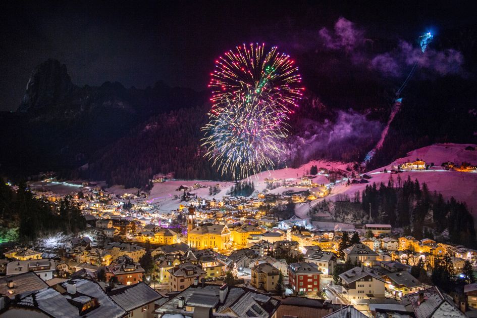 Fireworks exploding at night over a lit up Ortisei in the Val Gardena region of the Dolomites.