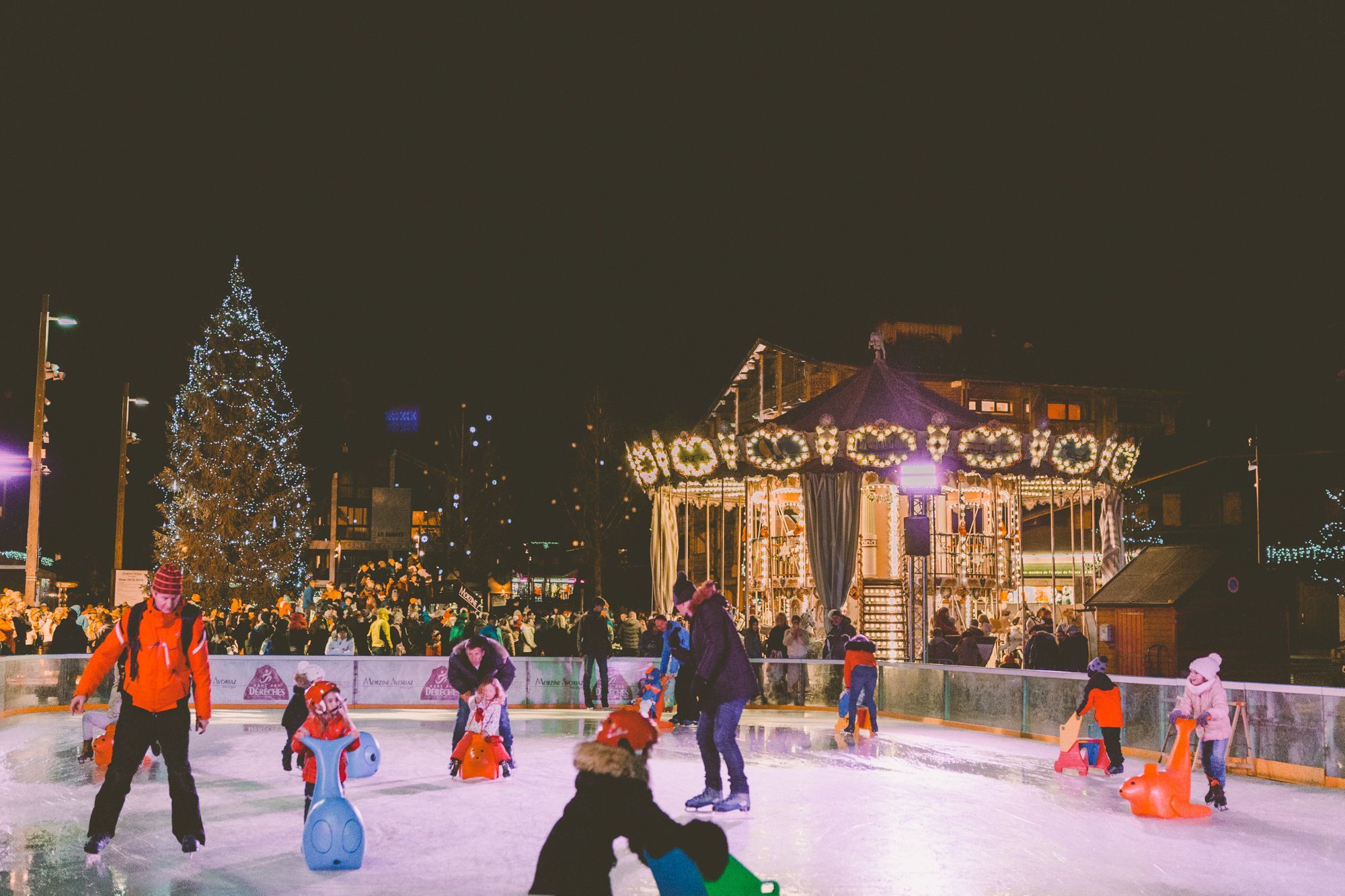 Christmas in Morzine. Image showing families ice skating in front of the Carousel and Christmas tree.