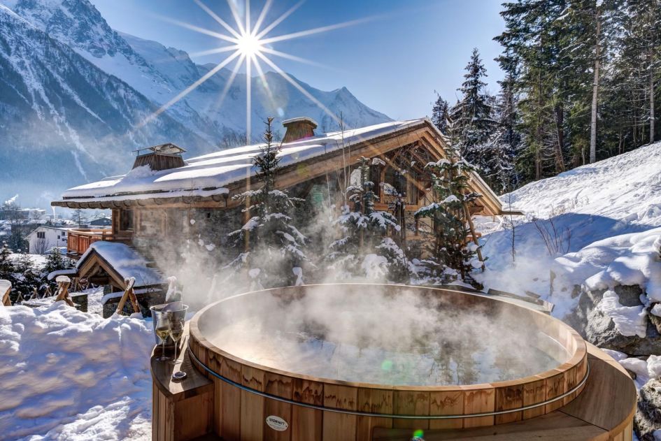 Outdoor cedar wood hot tub in the snow outside Chalet Azurite with a view of the mountains and sunshine 