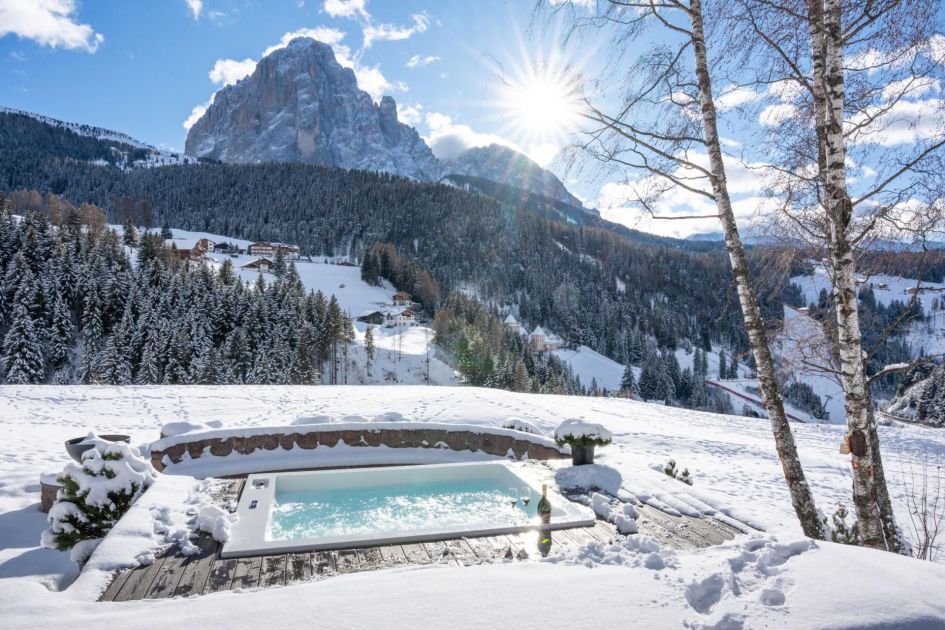 Sunken outdoor hot tub at Chalet Villa Carolina with a view of the iconic Dolomiti landscape and the sun pushing between the clouds