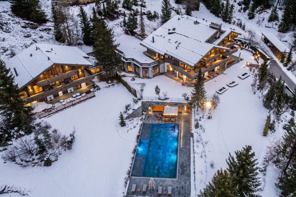 Aerial shot of Ultima Crans Montana, a luxury ski chalet in Crans Montana, Switzerland. Shown are two luxury chalets and a stunning outdoor swimming pool surrounded by snow.