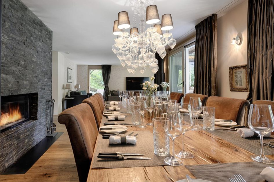 Dining table with a chandelier and fireplace in Chalet White Pearl, Zermatt. Great for family and friends meals from a private chef on a catered ski holiday in Switzerland