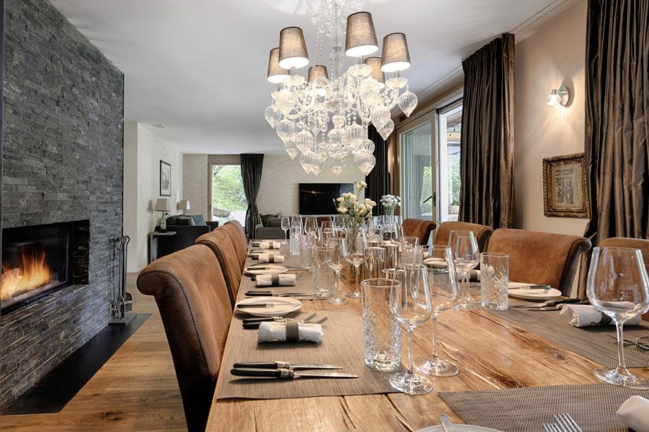 Dining room of Chalet White Pearl, Zermatt Dining table with a chandelier and fireplace in Chalet White Pearl, Zermatt. Great for family and friends meals from a private chef on a catered ski holiday in Switzerland