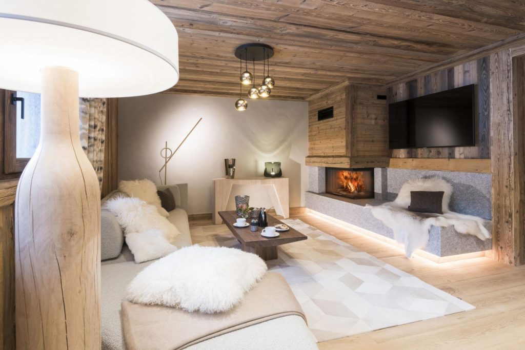 Living room of Chalet Carline, a luxury ski chalet in Saint-Gervais. The fireplace is roaring, and there are beautiful, modern furnishings and fluffy pillows. The room is cosy and stylish.