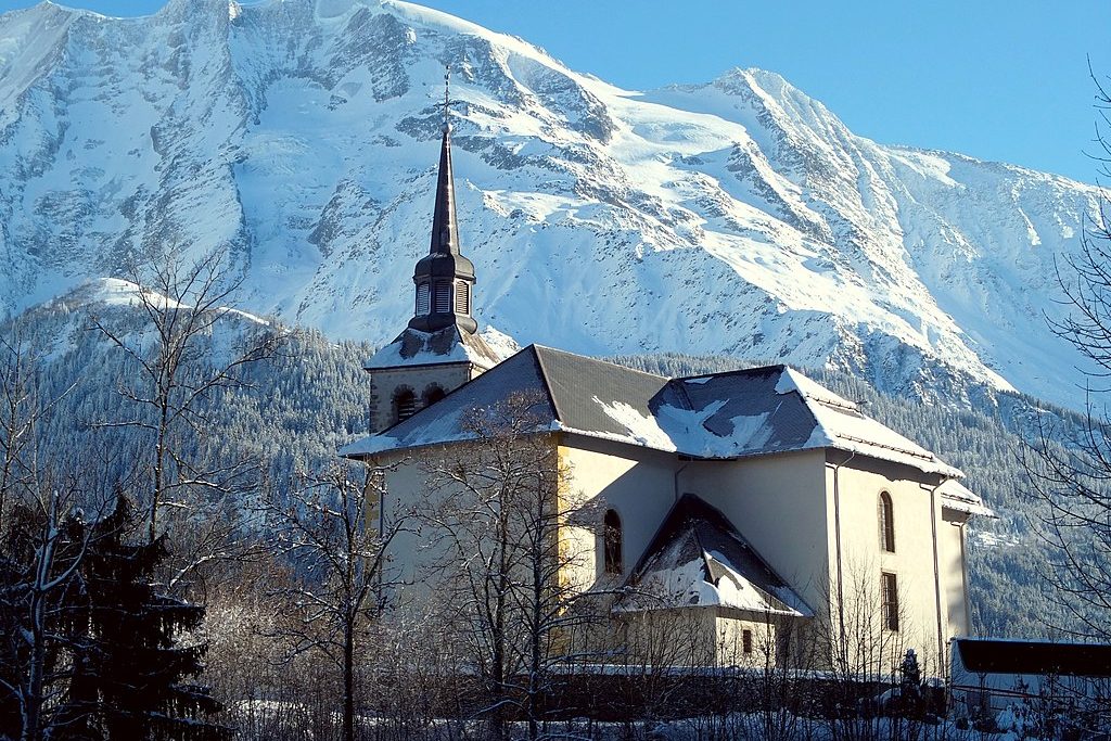 The beautiful Baroque church in Saint-Nicolas-de-Véroce, a petit village of Saint Gervais, one of the ski resorts near Mont Blanc. Mountains in the background, and bare trees in the foreground.