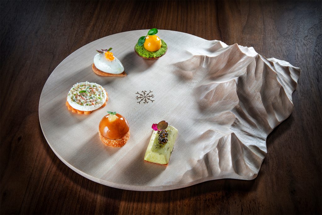 A mountain shaped serving dish with five different small food items, presented beautifully at this luxury restaurant in Saint-Gervais.