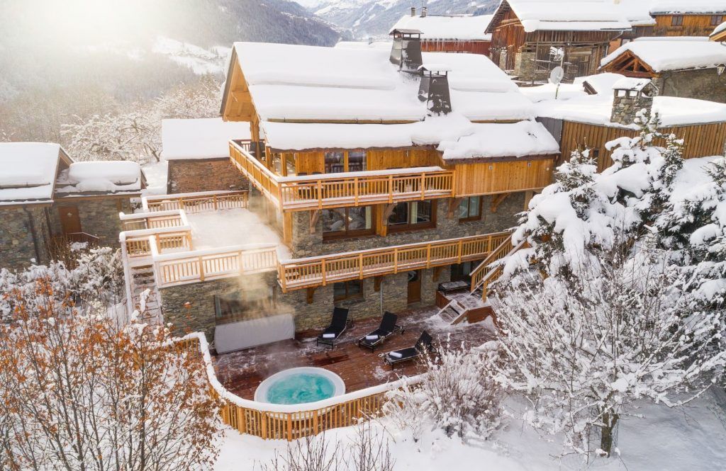 Exterior of Chalet Iona in Meribel, with a hot tub and surrounded by snowy trees, the ideal ski holiday for escapism