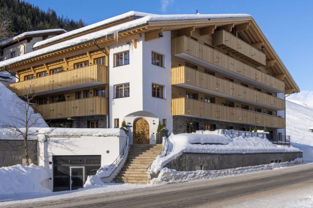 Exterior of Brunnenhof Residence, Lech, showing the spacious balconies and snowy scene behind this luxury ski accommodation.