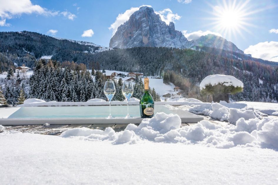 Outdoor hot tub at chalet Villa Carolina with Champagne on the side and a sunny, snowy mountain view.