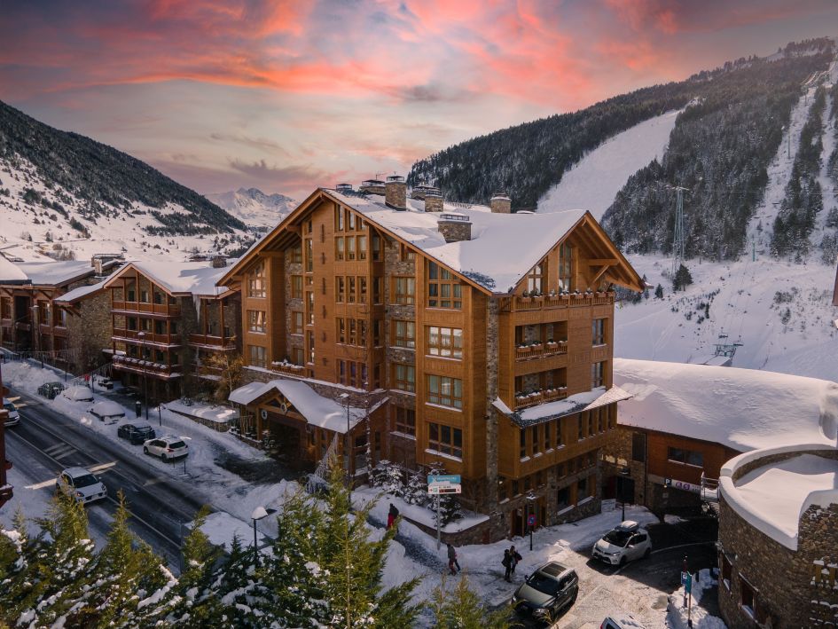 Exterior of Hermitage Mountain Residence, a luxury ski holiday residence in the Alps, located in Soldeu, Andorra. Backdrop of mountains, chairlift, and sunset.