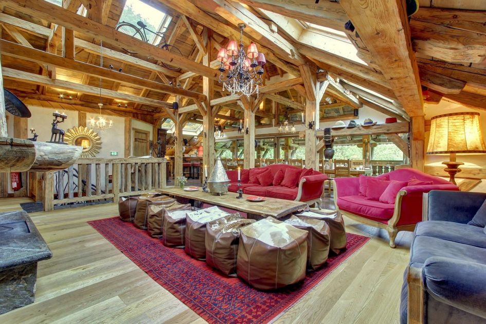 Table in the centre of Ferme du Lac Vert's main living area, surrounded by brown bean bag chairs, as well as red and blue sofas. An old farmhouse, this space still has high ceilings and exposed wooden beams, as well as plenty of natural light.