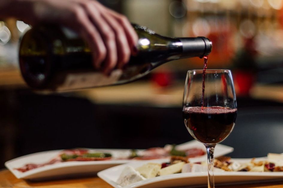 A person pours a glass of red wine in front of cheese and meat platters at Le Coup de Couer - one of the best restaurants to eat out in Morzine.