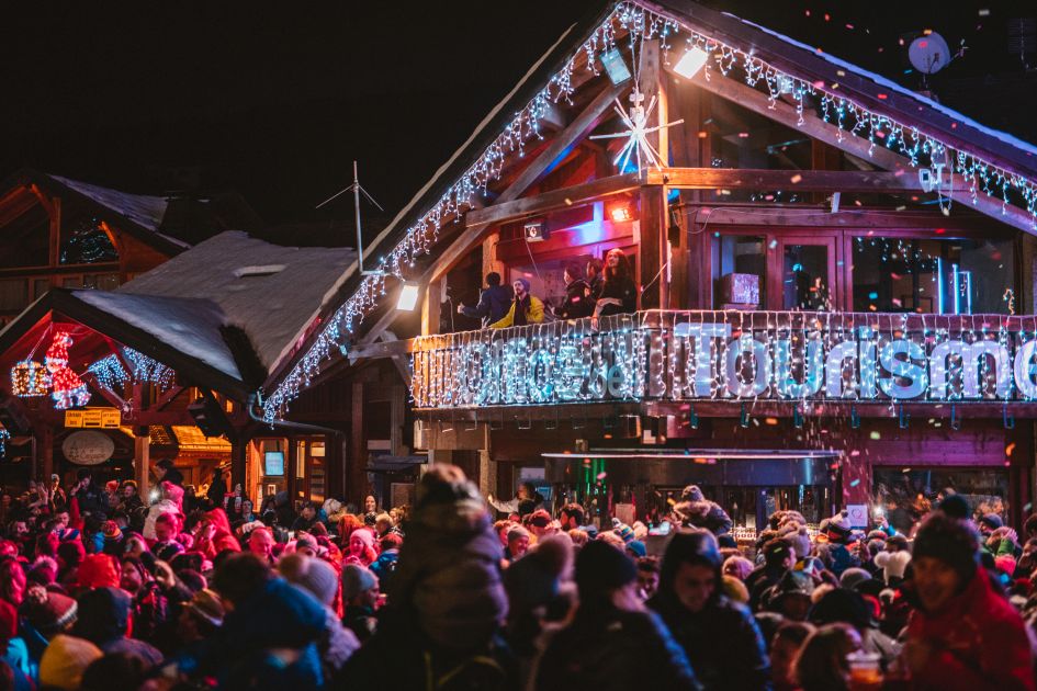 A picture of a well-lit Morzine tourist office, lit up by fairy lights at Christmas and surrounded by crowds of people.