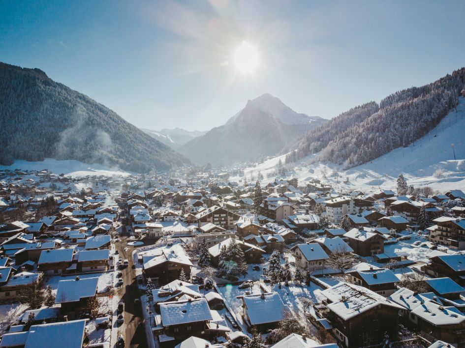 A sunny view over Morzine ski resort, with its snow-topped wooden chalets and the Nyon mountain in the background.