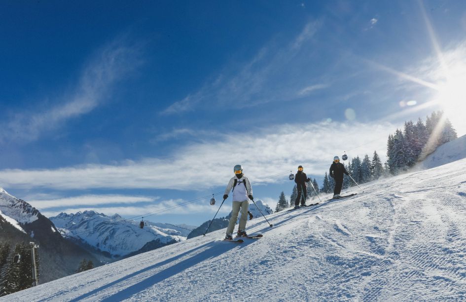 3 skiers stop for a picture on one of Morzine's slopes on a blue, sunny day. Cable cars and mountain peaks can also be seen in the distance.