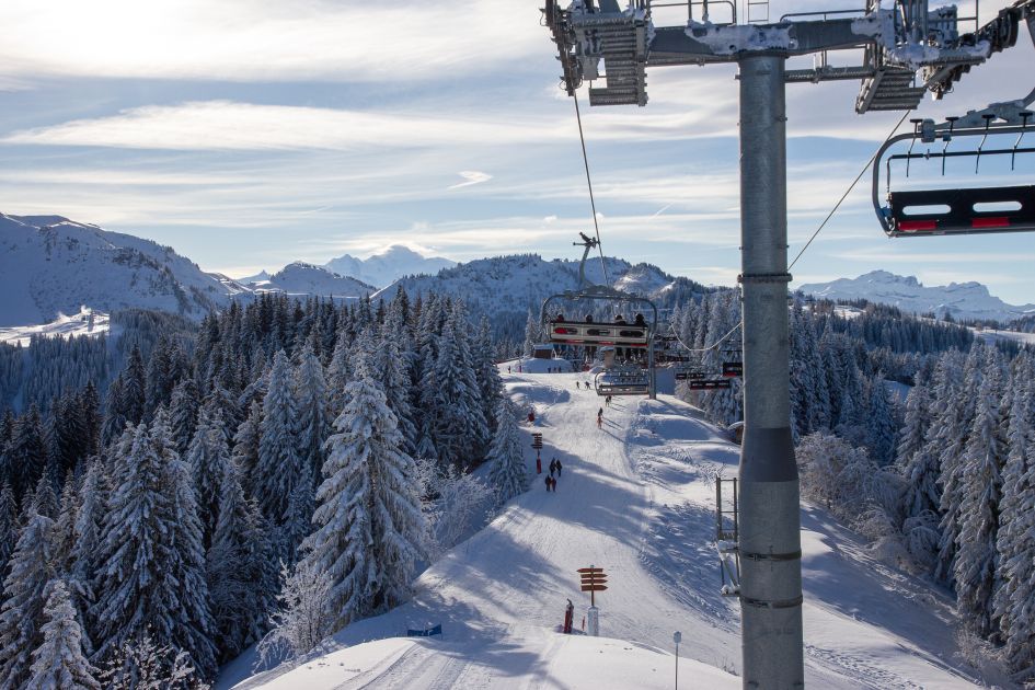 View from a chairlift in Morzine looking down to skiers on the piste below, surrounded by snow-covered trees and views out to the mountain peaks in the distance.