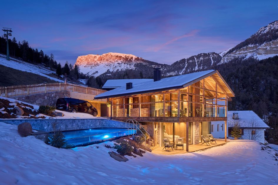 Chalet Vilaiet, Ortisei. Exterior shot of one of the best family ski chalets in Italy, Chalet Vilaiet, and its outdoor swimming pool at dusk.
