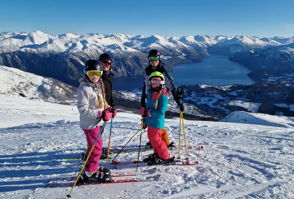 Fran, Andy and their girls enjoying a family ski holiday in the mountains. Positioned on the piste with a mountain and lake view on a bluebird day. 