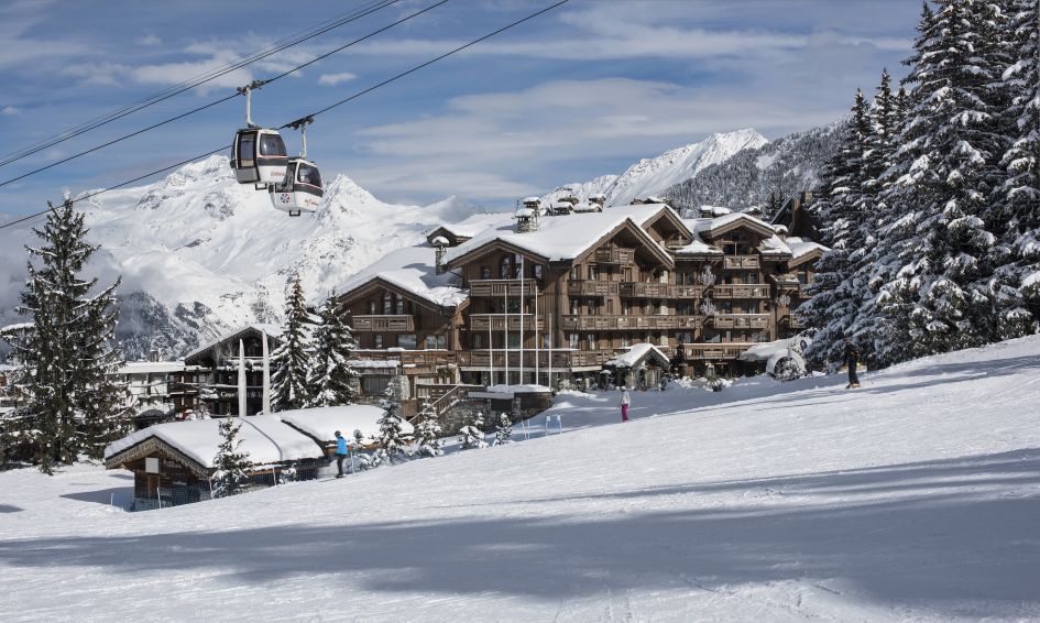One of the best luxury ski hotels in Europes, Grandes Alpes, seen here on the edge of the Croisette in the centre of Courchevel 1850. Skiers and gondola cabins pass by in the foreground. 
