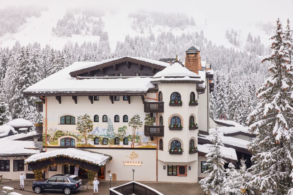 A snowy exterior of Hotel Les Airelles Courchevel, with snowy trees and slopes in the background.