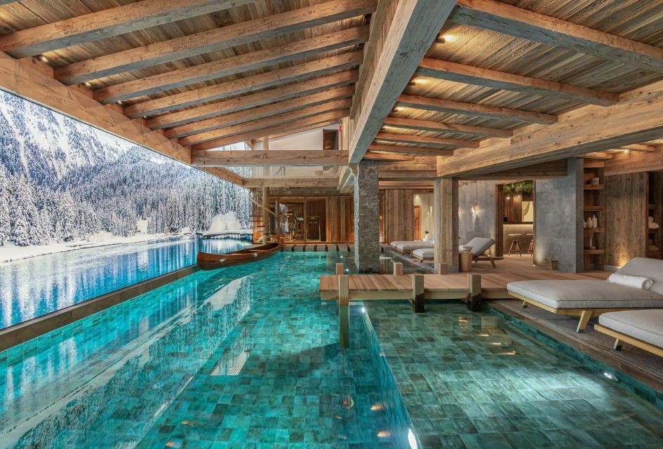 The incredible indoor swimming pool at Chalet Bruxellois in Courchevel 1850 with a mini jetty, wooden canoe boat featre and serene winter lake scene to swim before. 