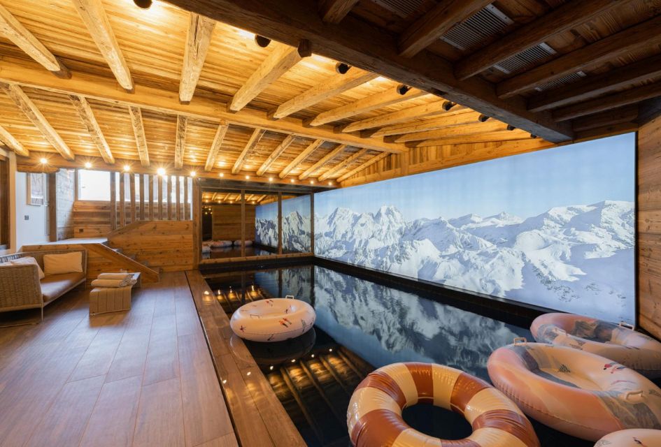 Indoor pool at Chalet Le 1550, Courchevel Village Interior pool of Chalet Le 1550 in Courchevel Village, surrounded by traditional alpine wood and a screen displaying mountain scenes.