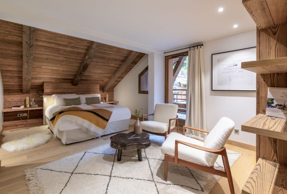 Apartment Nanuq, Méribel Chic bedroom at Apartment Nanuq, plush furnishings encompassed by neutral tones and complimenting wooden features to encompass a traditional alpine style with a modern twist. Plenty of natural light seeps in from the large door-winow that leads out onto a balcony.