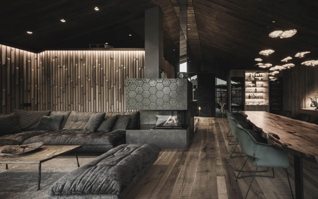 Chalet Vilaiet, Ortisei An open-plan living and dining area with warm lighting and a dual aspect fireplace