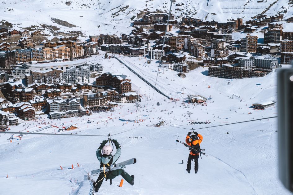 La Bee tyrolienne, a double zipline, with two passengers ziplining over the ski slopes into the resort of Val Thorens.