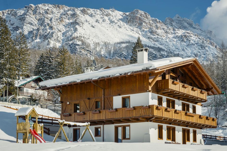 LV | 01 Dolce Vita, Cortina Spacious chalet in Cortina with the mountain scape in the background, a childrens playground is visible outside the chalet