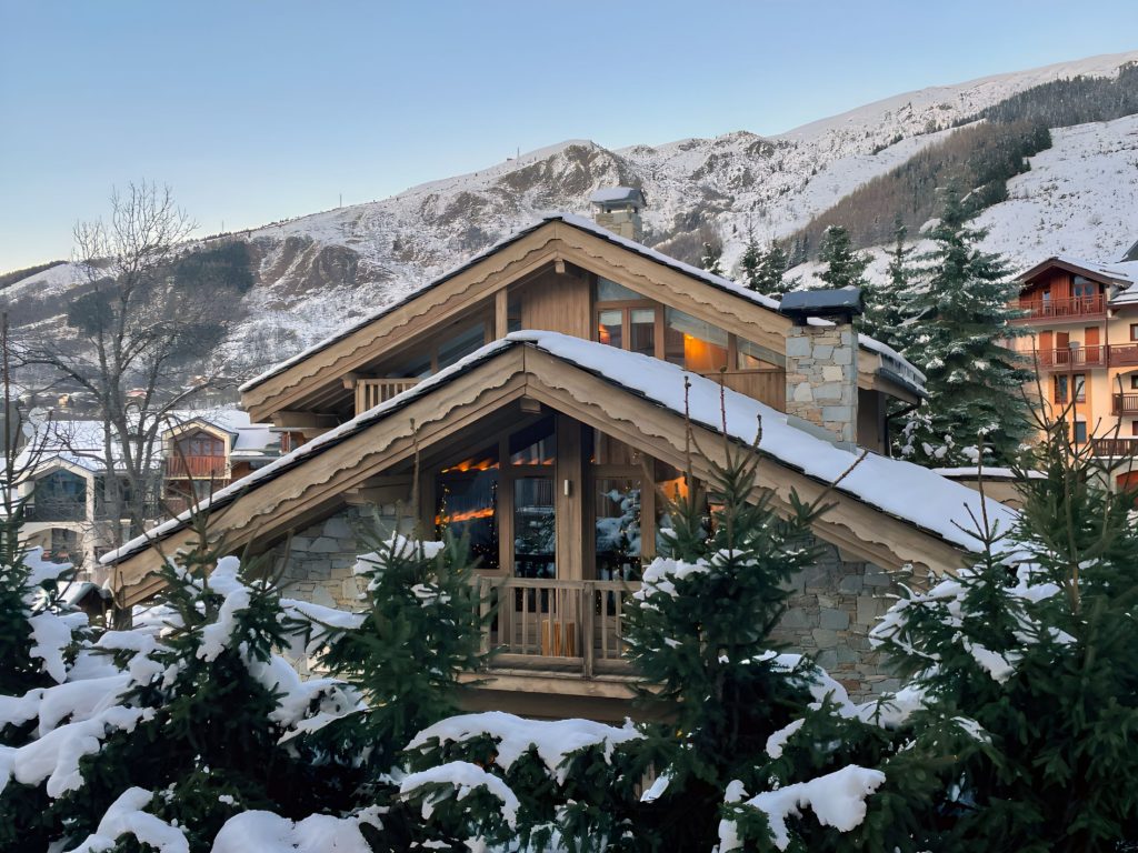 Grande Chalet Floralie, St Martin de Belleville A large, rustic Grande Chalet Floralie covered in snow, set against a backdrop of St Martin de Belleville.