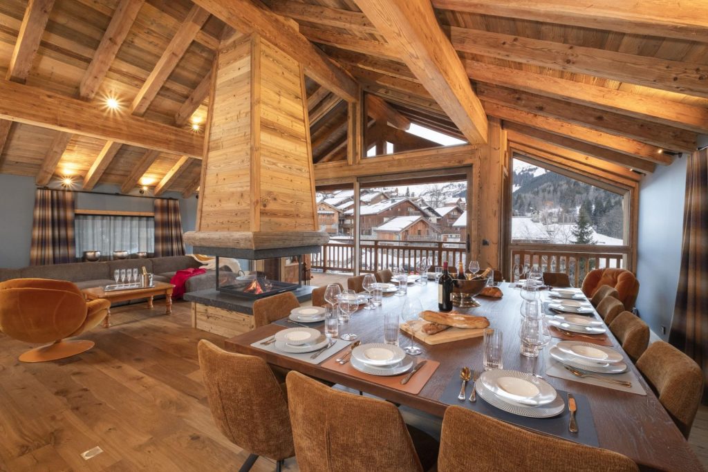 Grand Chalet Kalinka, Méribel Chalet Kalinka's living space, featuring an open-plan design, vaulted ceilings, exposed beams, and an alpine atmosphere. Floor-to-ceiling windows frame the valley.